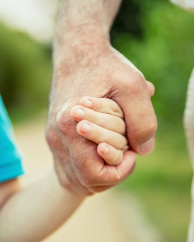 Child holding hand of senior man over a nature background. Two different generations concept.