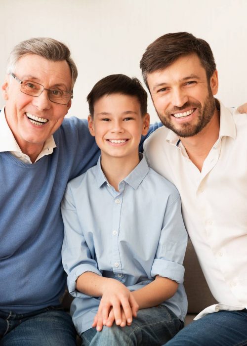 Male Generation. Happy Grandfather With Son And Grandson Smiling At Camera Hugging Sitting Together On Couch At Home.