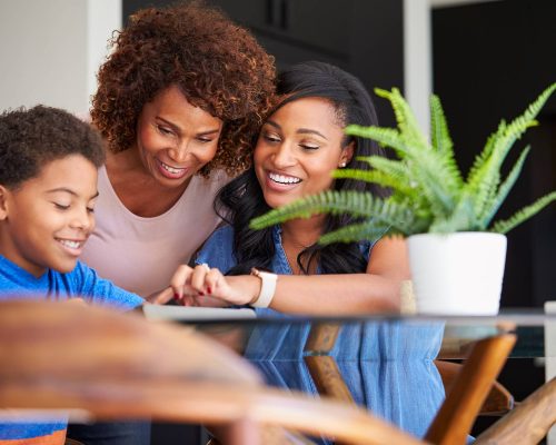 Grandmother With Mother Helping Grandson To Do Homework On Digital Tablet